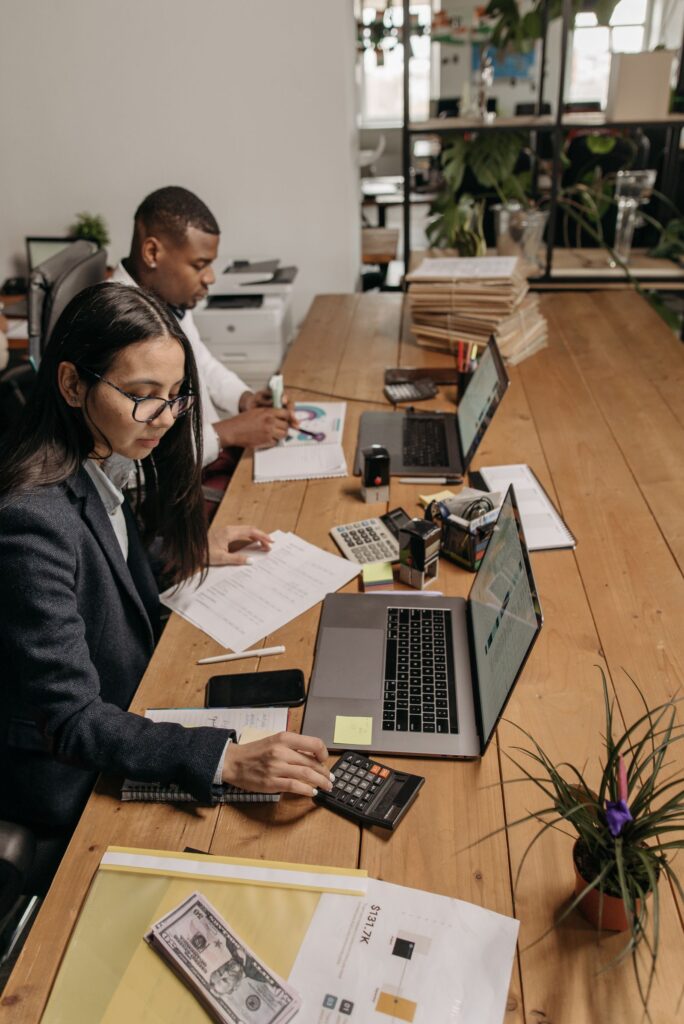 Two accountants working at a shared office table with laptops
